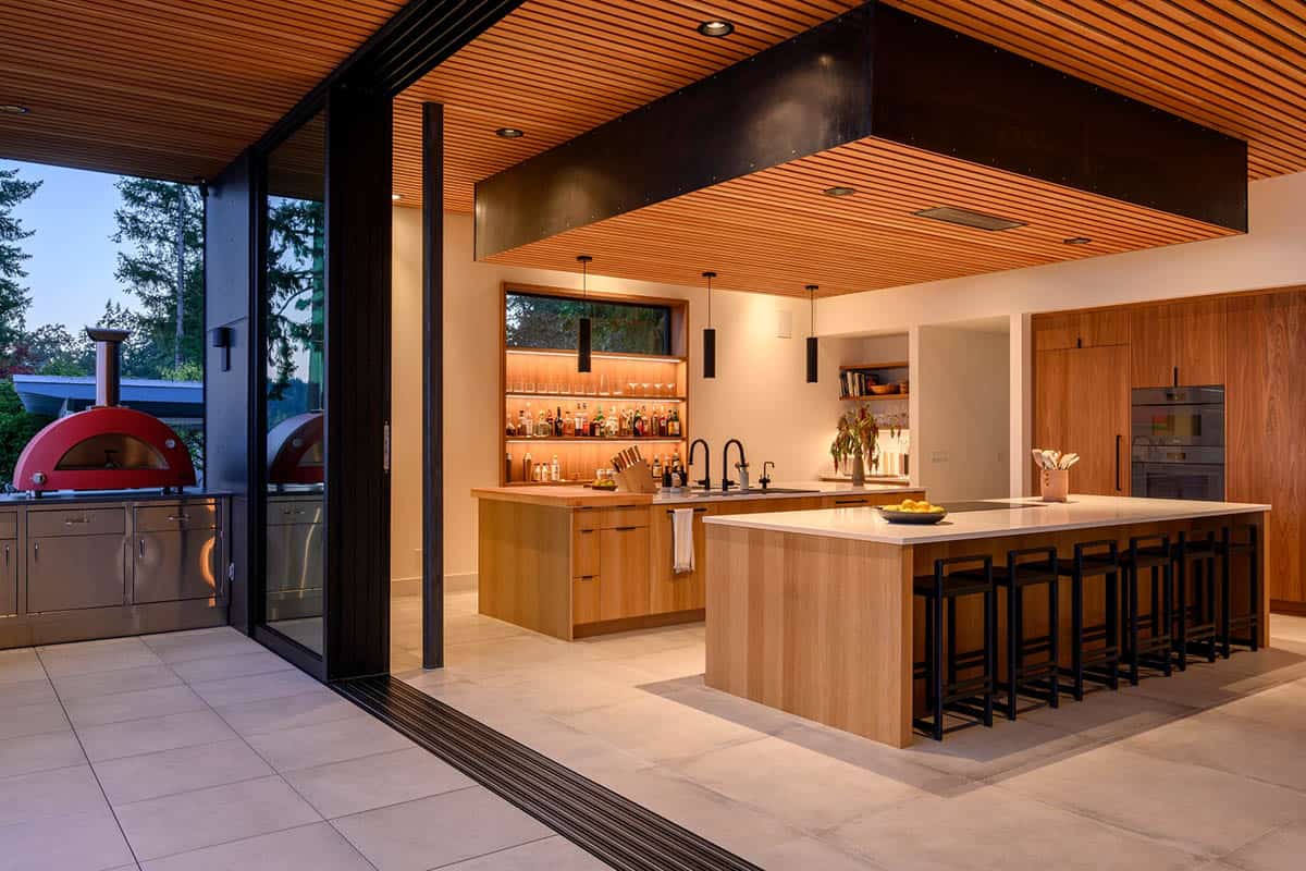 Outdoor kitchen with red pizza oven beside slatted wood ceiling
