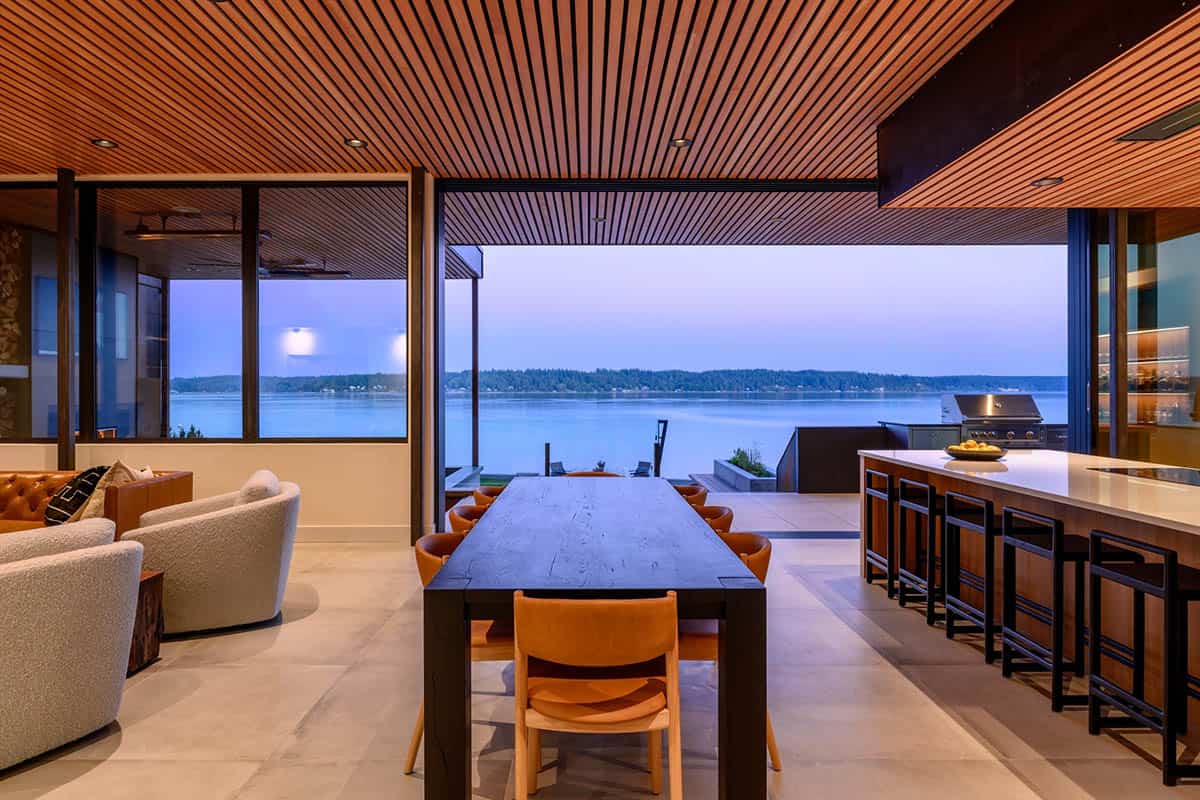 Dining table set beneath wood ceiling overlooking dusk water view
