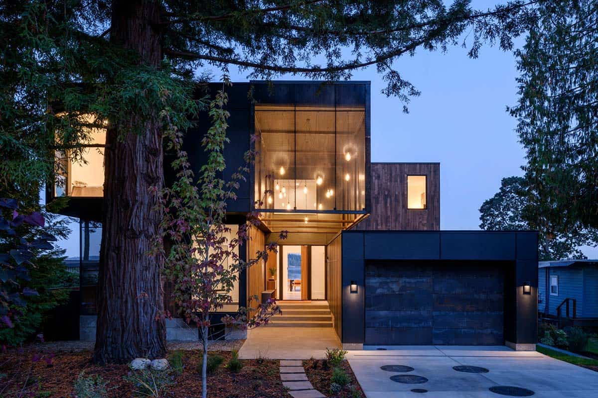 Illuminated black facade glows at dusk beneath tall redwood tree