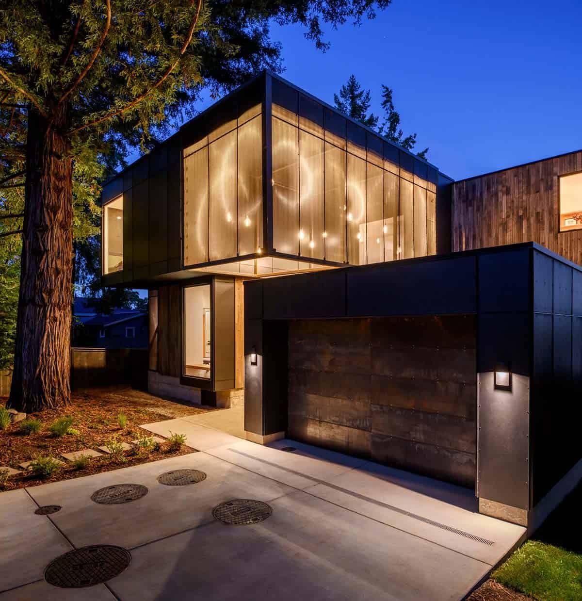 Black metal facade lit at night beside corten garage door
