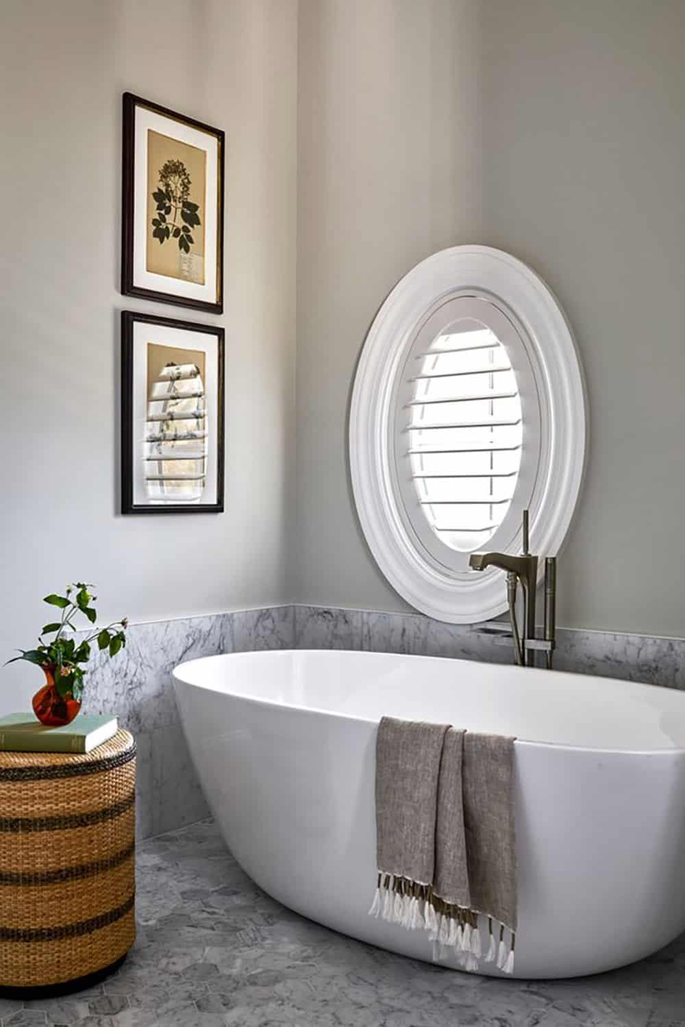 Freestanding oval soaking tub beneath an arched shuttered window