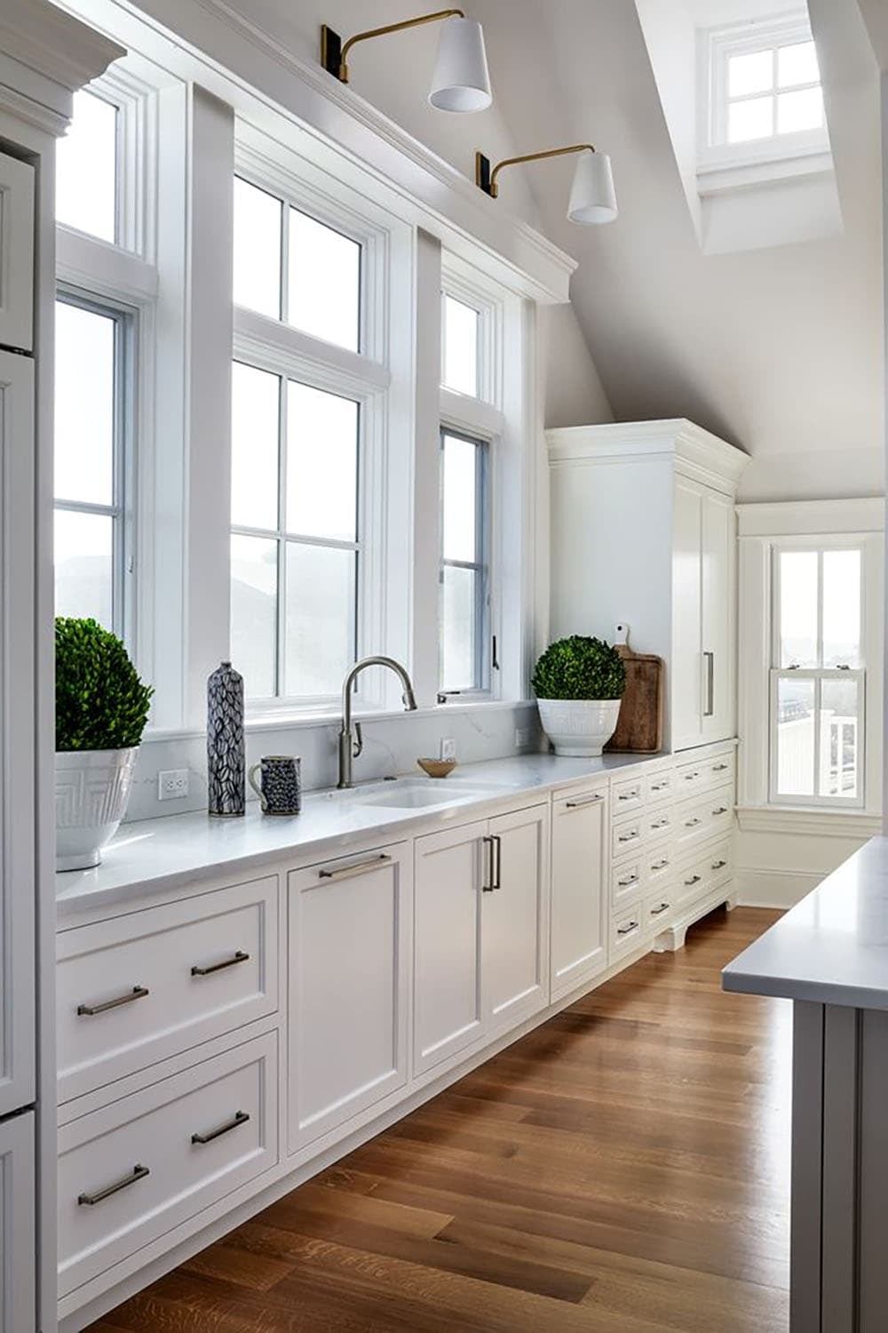 Long white kitchen counter lined with windows and brass sconces