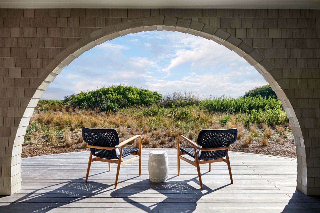 Shingled archway framing dune grass and two woven armchairs