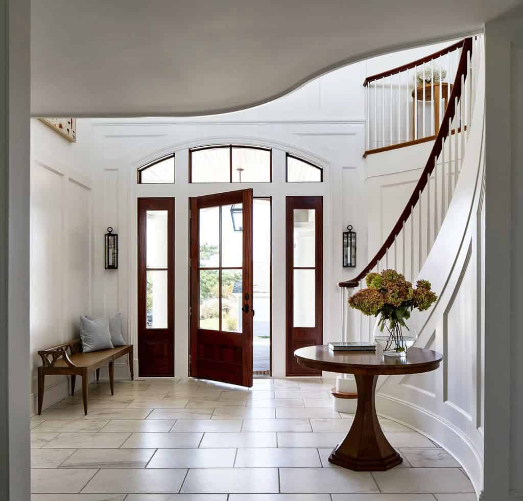 Curved staircase and arched wood door in marble-floored foyer