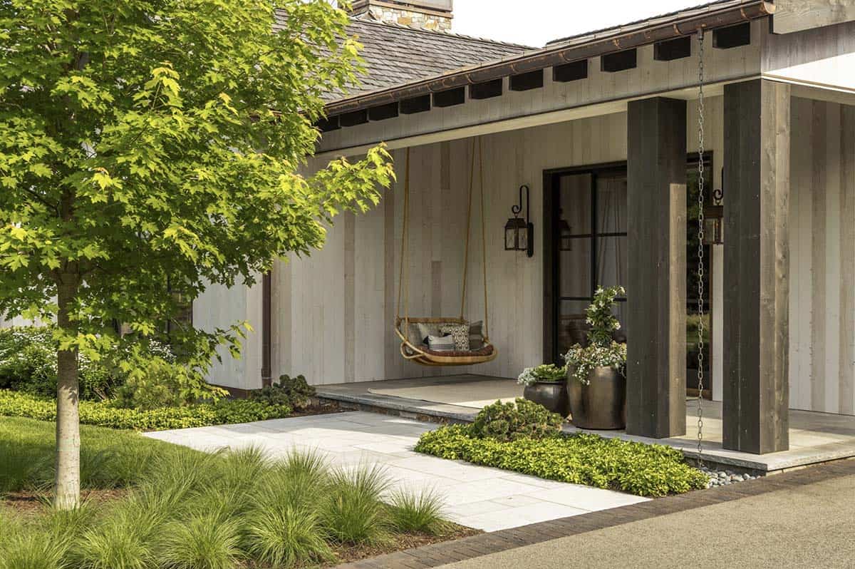 Covered front porch with woven swing, dark timber columns, and stone walkway