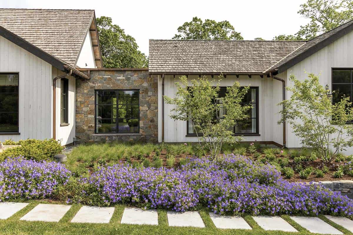 Exterior detail of stone chimney base, black-framed windows, and purple flowering landscaping
