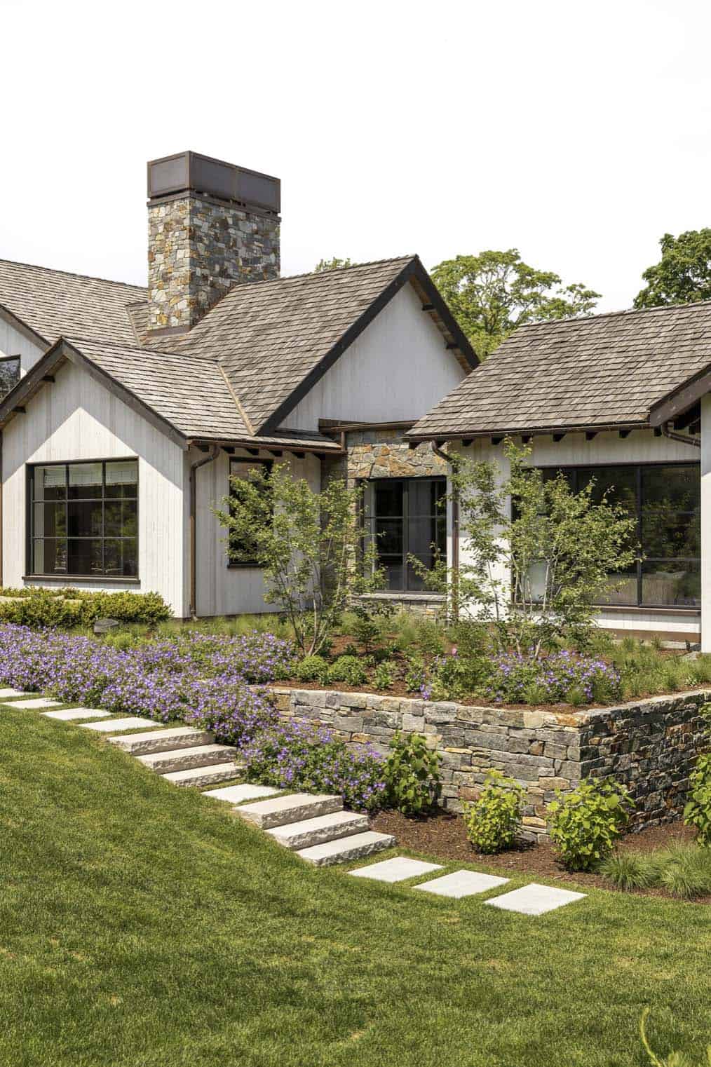 Close-up of gabled rear facade with stone chimney and terraced garden beds