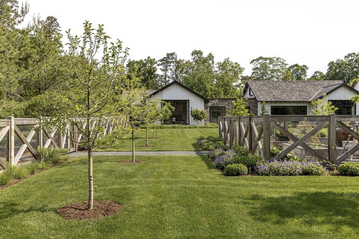 Side yard with wood picket fence, young trees, and view toward the home's gabled wing