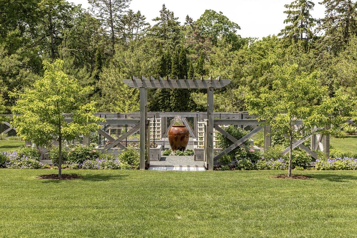 Wooden pergola entrance to the fenced kitchen garden with large ceramic urn fountain
