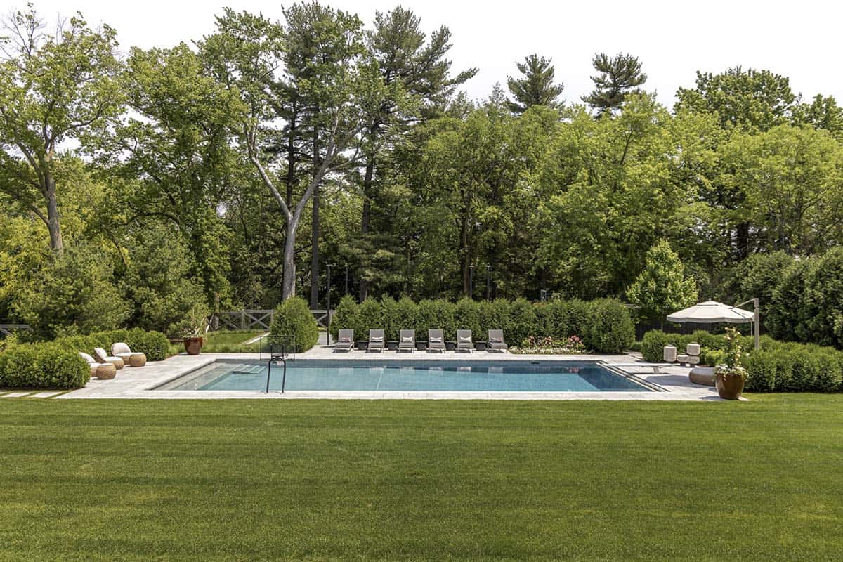 Rectangular pool with stone deck, lounge chairs, and hedge screening