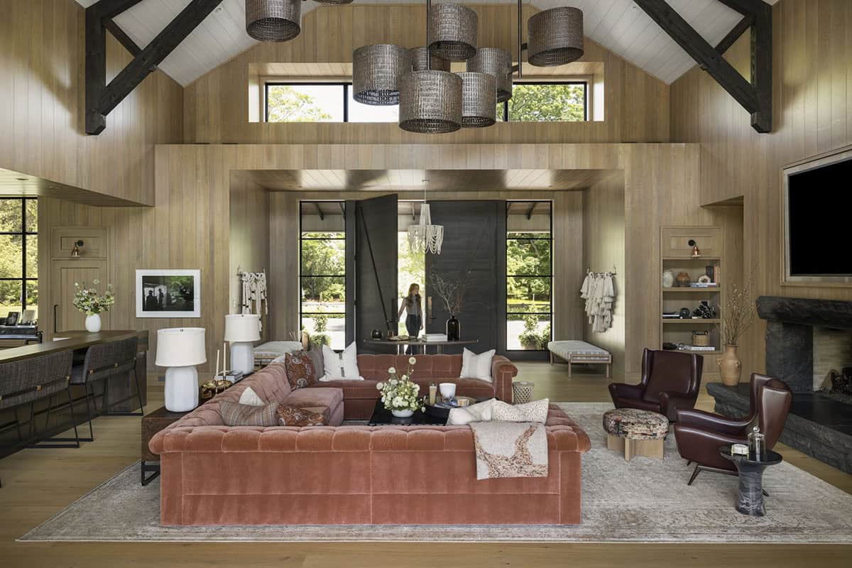 Vaulted great room with wood paneling, exposed beams, and sectional sofa facing black entry doors