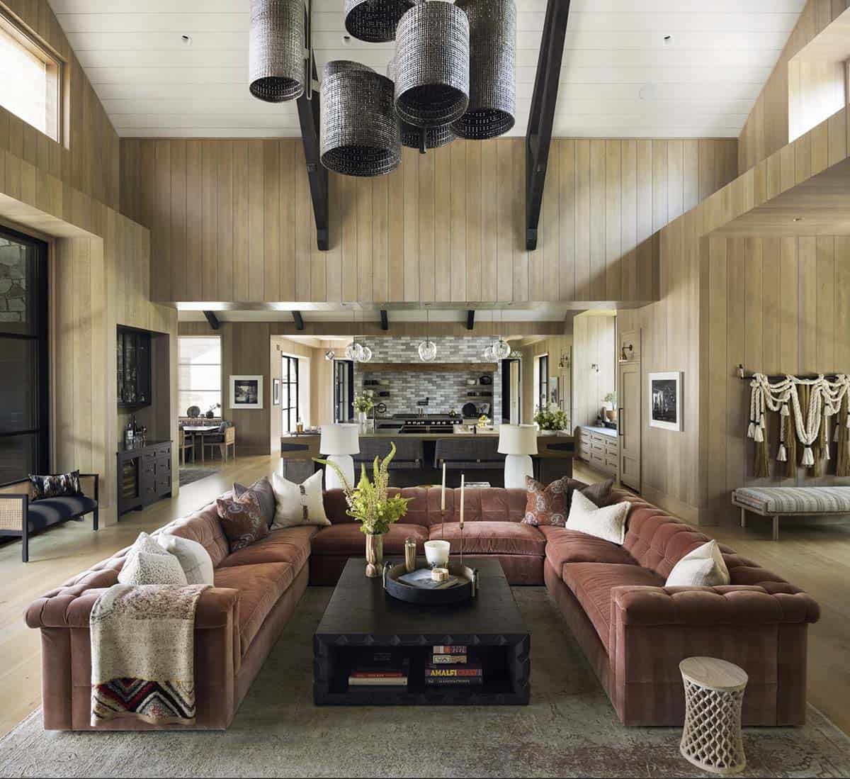 Great room with rust-colored sectional sofa, cylindrical pendant lighting, and open kitchen beyond