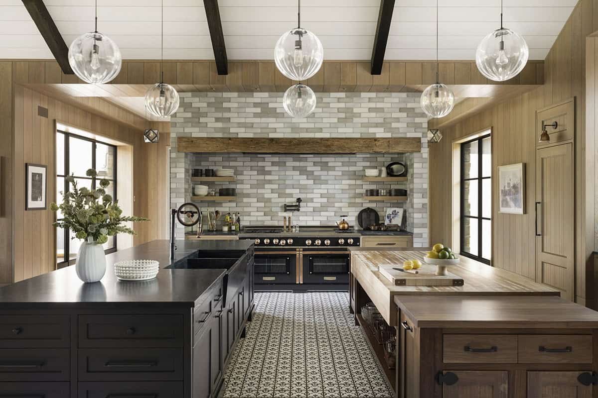 Kitchen island seating with brass fixtures, patterned tile floor, and dark cabinetry facing a tiled range wall