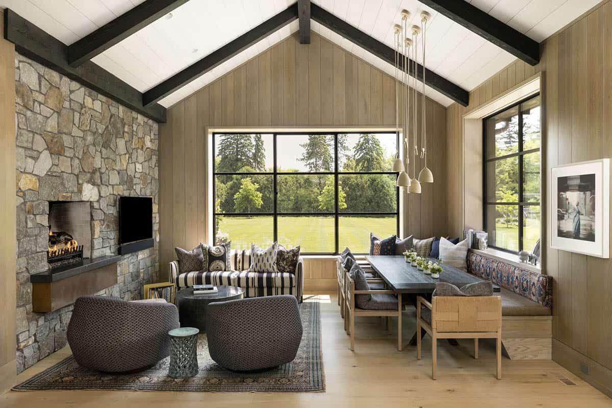 Sitting room with stone fireplace, patterned sofa, and dining bench beside a large picture window