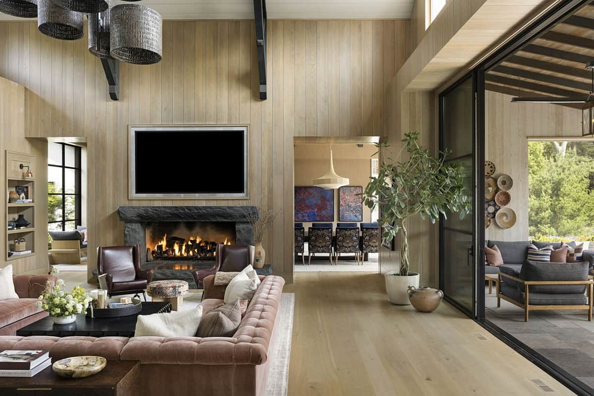 Living room with stone fireplace, velvet sofa, and open sightline to dining room and covered porch