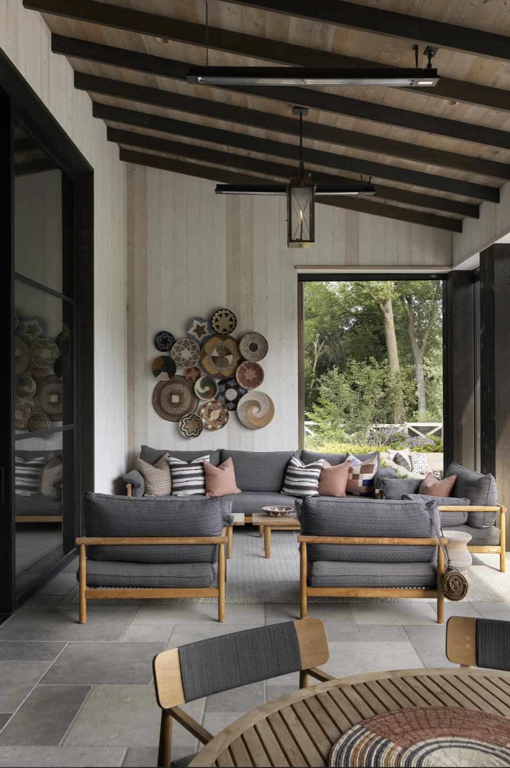 Covered porch seating area with gray lounge chairs, decorative basket wall art, and heat lamps