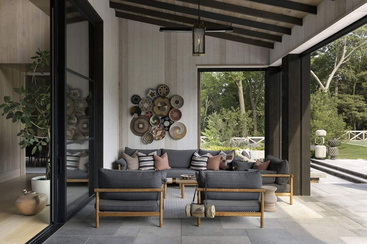 Covered patio lounge with woven furniture, basket wall display, and open view to trees and tennis court