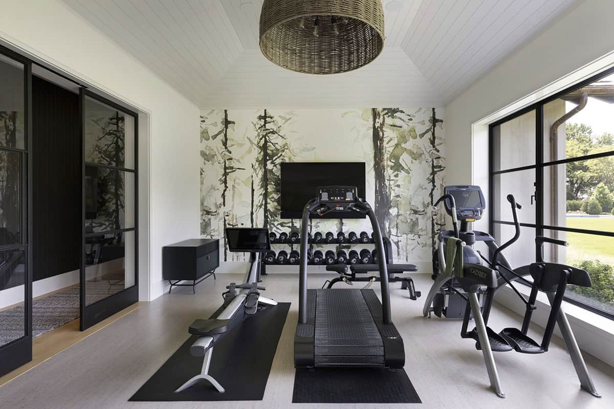Home gym with treadmill, weight rack, forest-themed mural, and woven pendant light