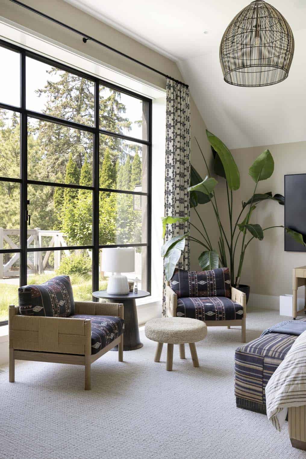 Bedroom sitting area with patterned lounge chairs, houseplant, and wire pendant light by a large window