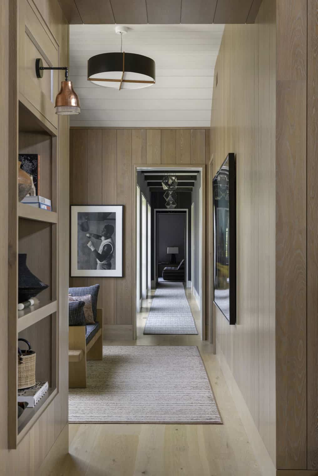 Wood-paneled hallway with boxer photograph, bench seating, and view toward a dark accent room
