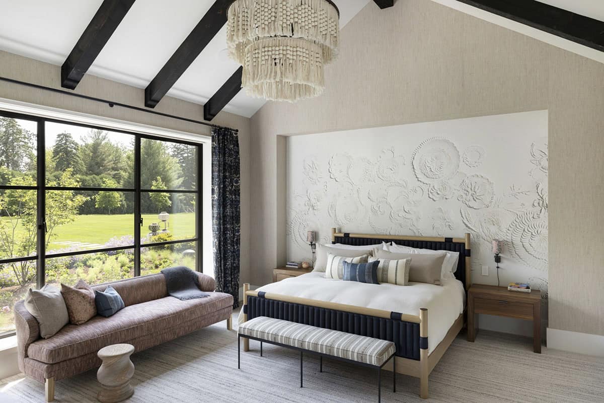 Primary bedroom with textured plaster headboard wall, beaded chandelier, and black ceiling beams