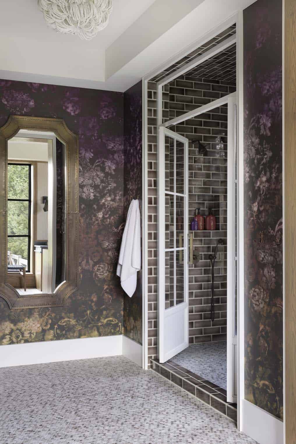 Bathroom with dark floral wallpaper, arched brass mirror, and tiled walk-in shower