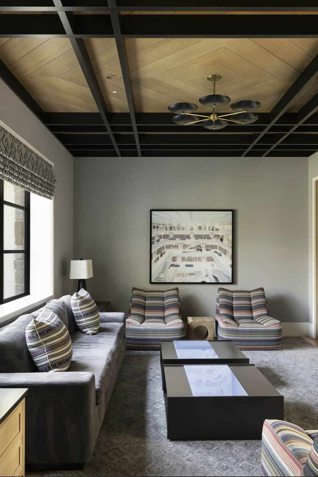 Media room with striped armchairs, gray sofa, coffered wood ceiling, and library photograph art