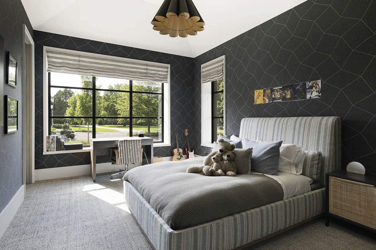Bedroom with dark geometric wallpaper, striped upholstered bed, desk, and sports memorabilia