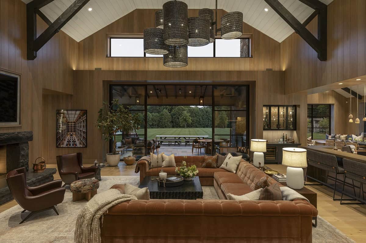Great room at dusk with tufted sectional, leather chairs, stone fireplace, and open sliding doors to patio