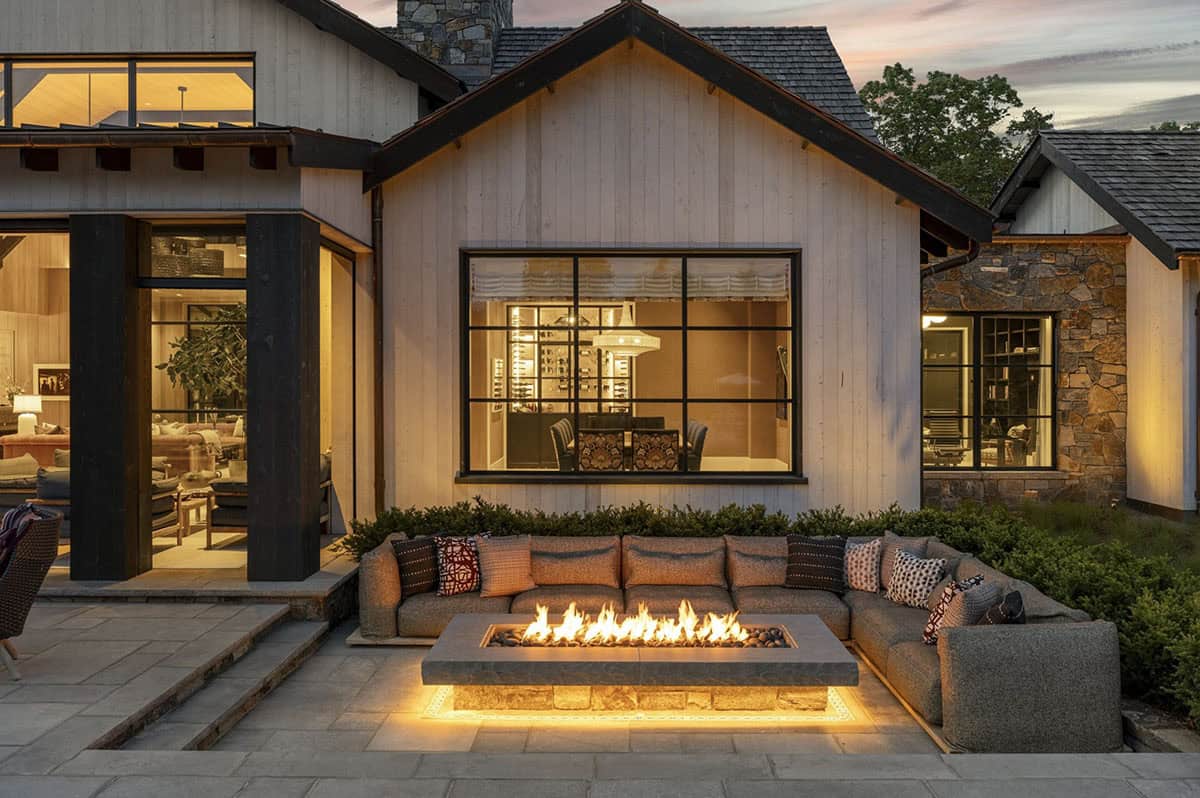 Outdoor fire pit lounge at dusk with sectional seating and glowing interior rooms visible through windows