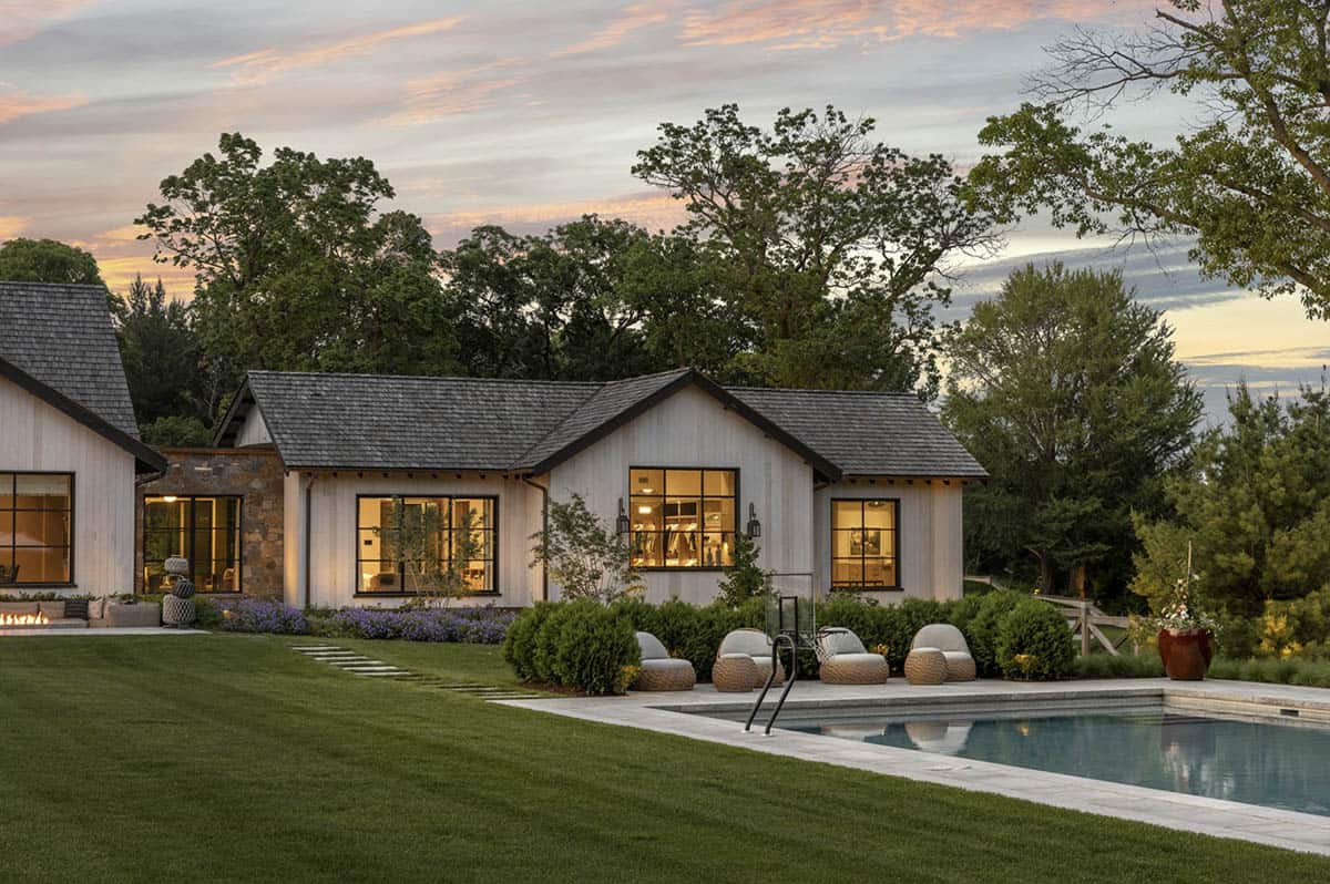 Pool at dusk beside gabled wing of the home with lit interior windows and lounge chairs