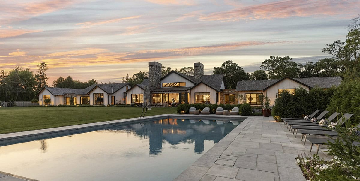 Wide dusk view of the home's rear elevation reflected in the pool