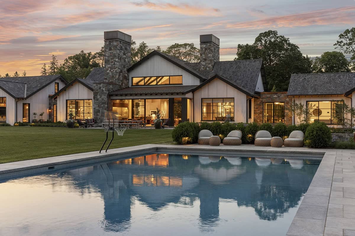 Rear exterior at sunset with basketball hoop, pool, and warmly lit great room windows