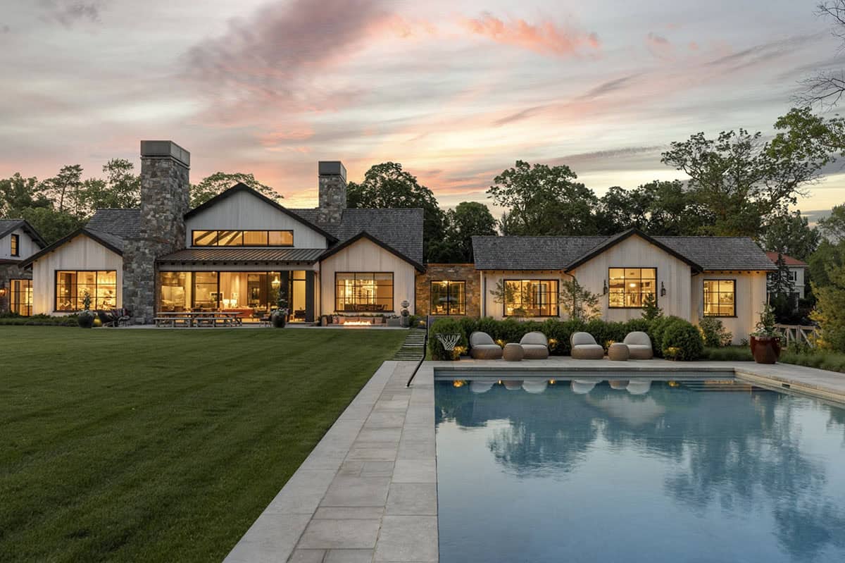 Pool and lawn at dusk with view of the home's multiple gabled rooflines and stone chimneys