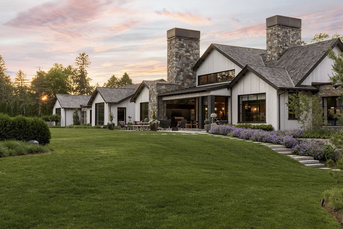 Side exterior at dusk with covered patio seating and purple flowering border along the lawn