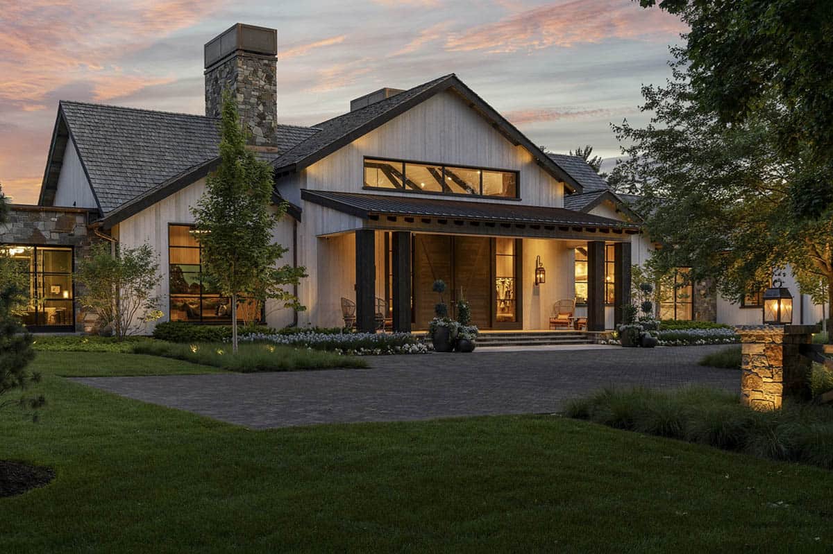 Front entrance at dusk with covered porch, wood double doors, and lantern sconces