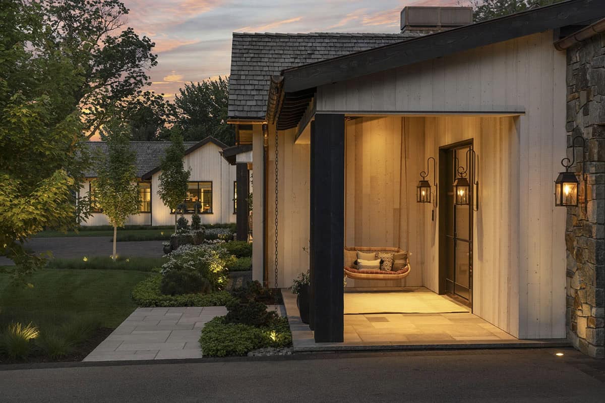 Side porch entrance at dusk with hanging swing, lantern sconces, and glass front door