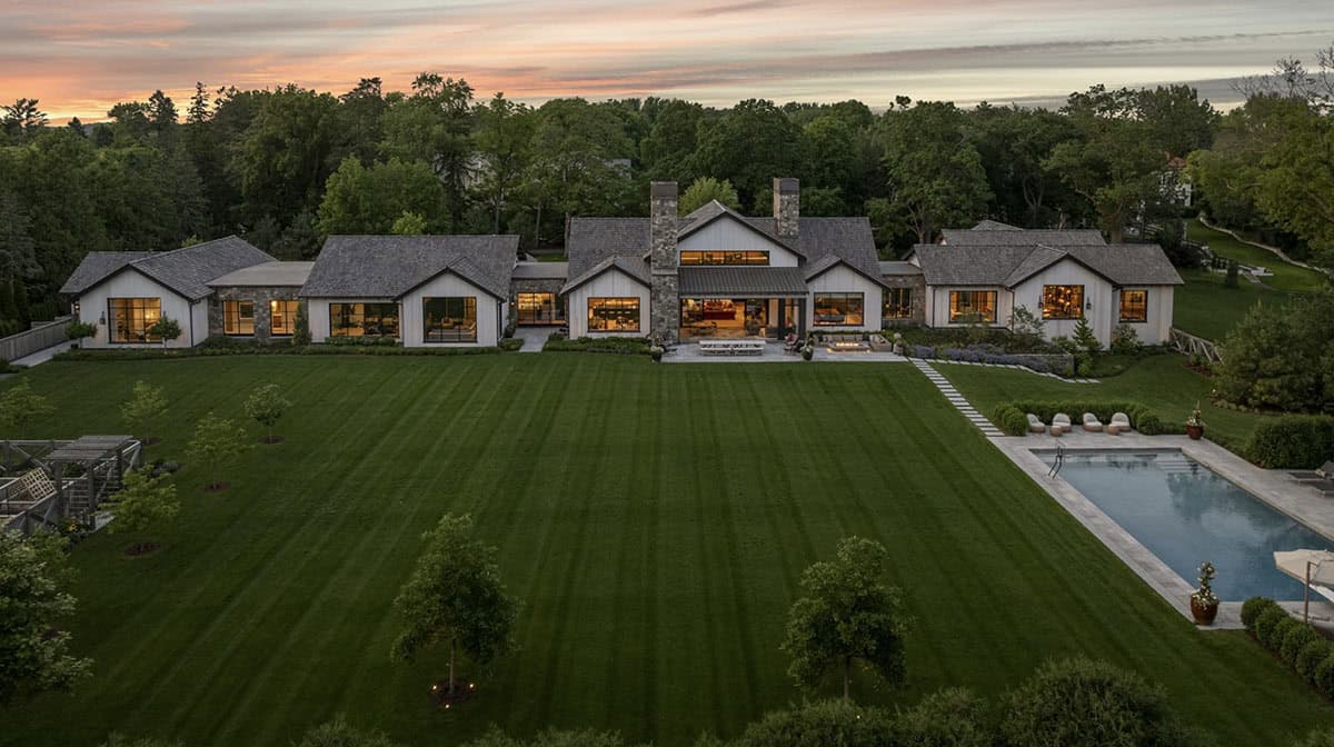 Aerial dusk view of the full home layout with pool, lawn, and warmly lit interiors