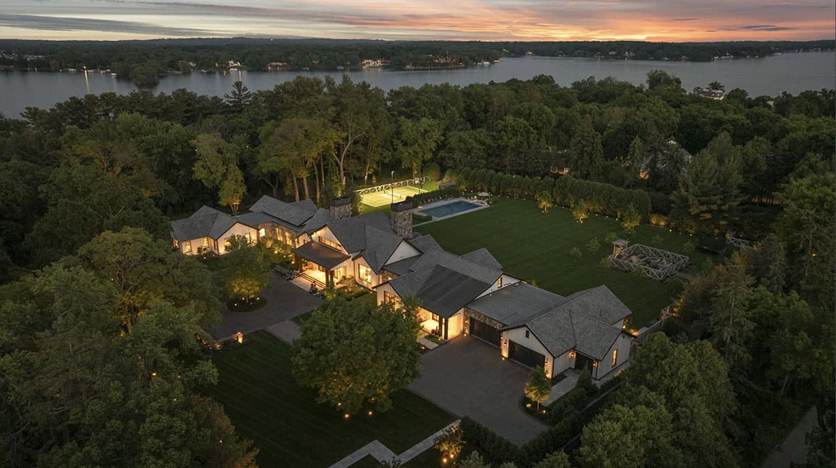 Aerial night view of the property with pool, tennis court, and lake in the background