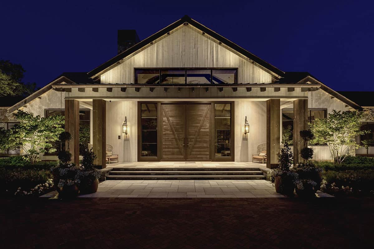Front entrance at night with wood double doors, timber porch columns, and lantern sconces