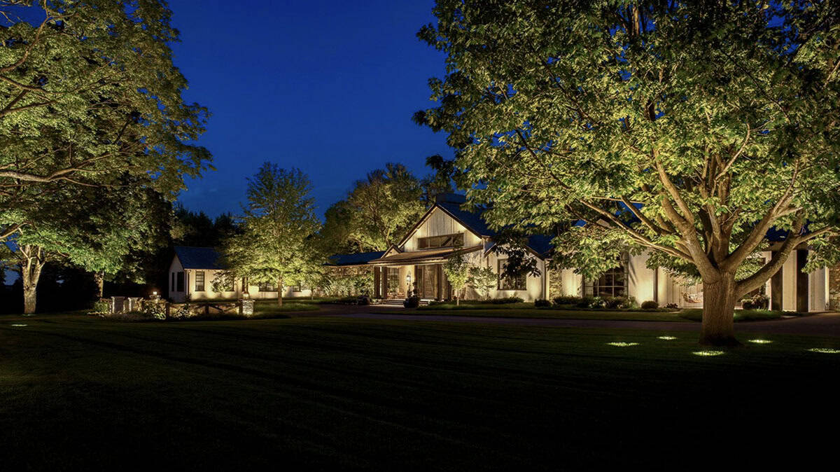 Nighttime view of the home's facade uplit by landscape lighting among mature trees