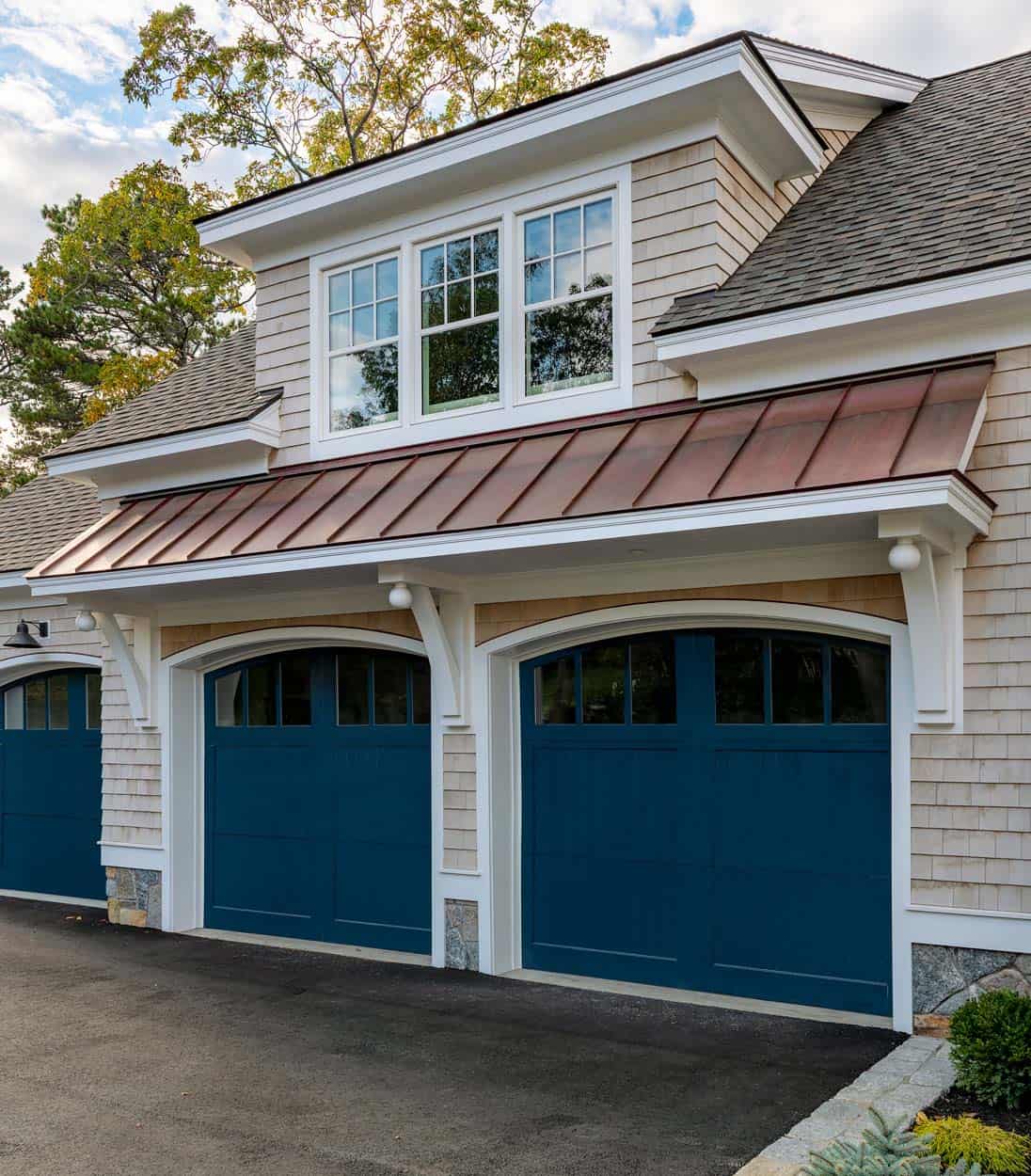 Copper roof overhang above navy garage doors on shingle-style home