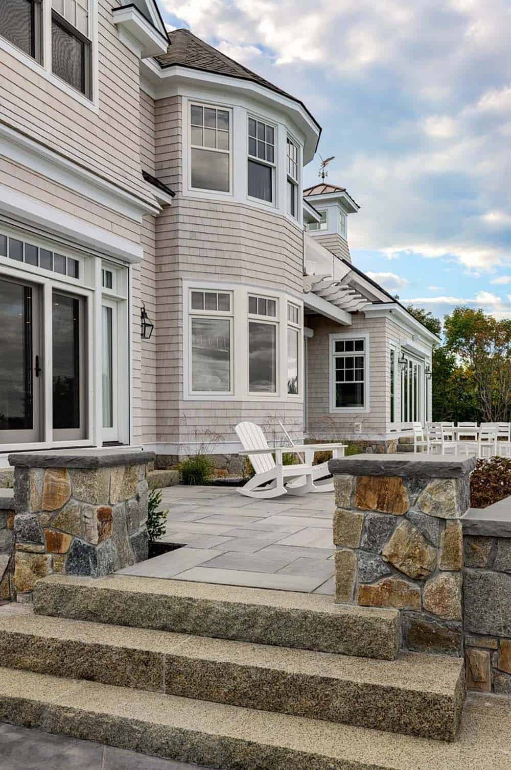 Stone-walled patio with white rocking chairs beside bay window addition