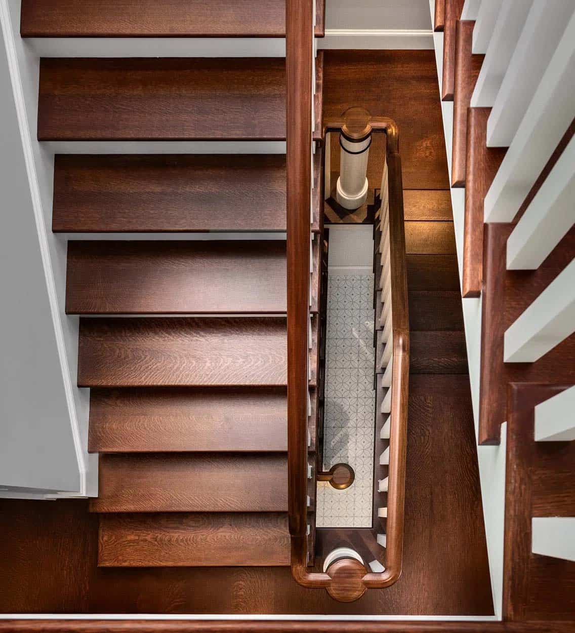 Overhead view of a wooden staircase spiraling down to patterned tile floor