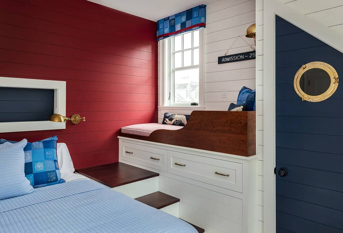 Built-in daybed nook with red shiplap wall and porthole-style door