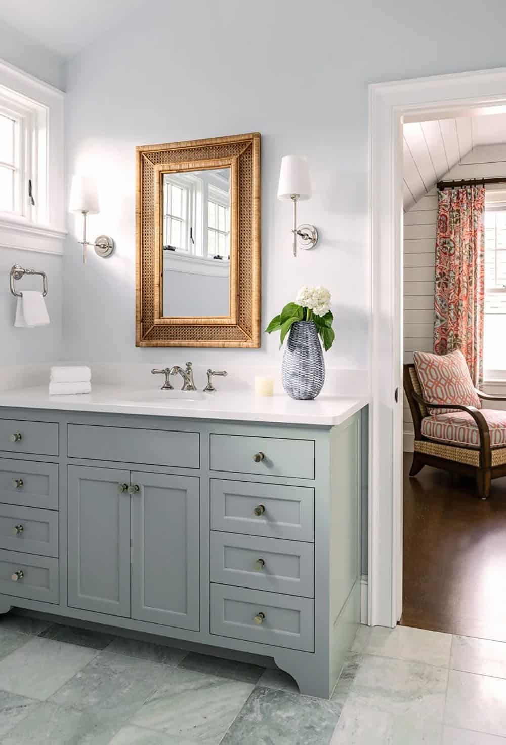 Bathroom with sage green vanity, rattan mirror, and marble floor tile
