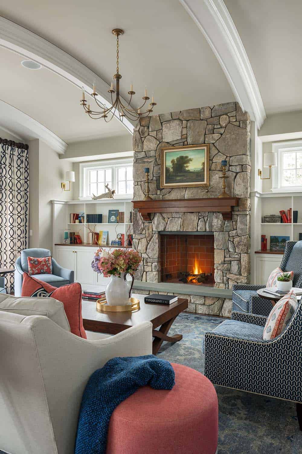 Living room with stone fireplace, chandelier, and blue-and-coral seating