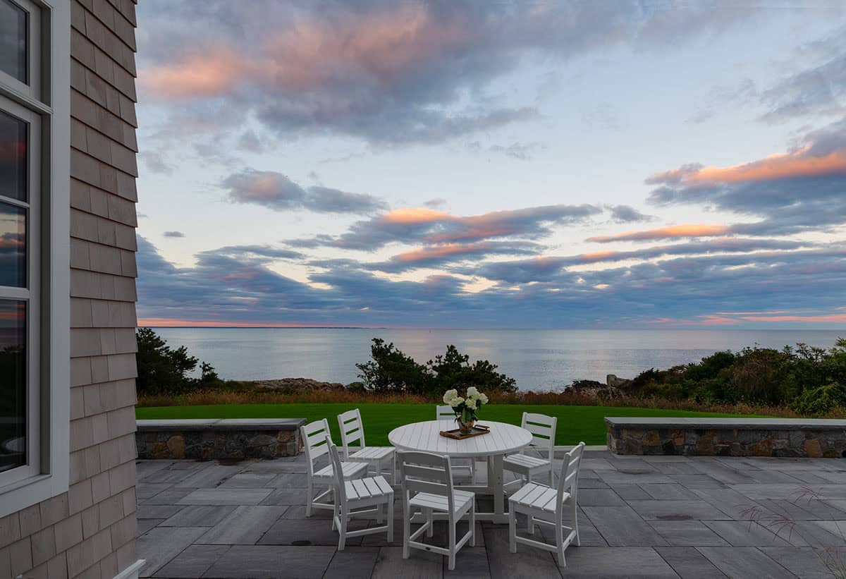 Stone patio with white dining set overlooking the ocean at sunset