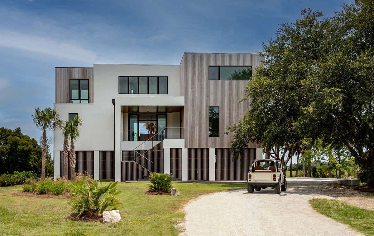 Modern coastal home exterior with wood siding, elevated design, and Jeep parked in gravel driveway