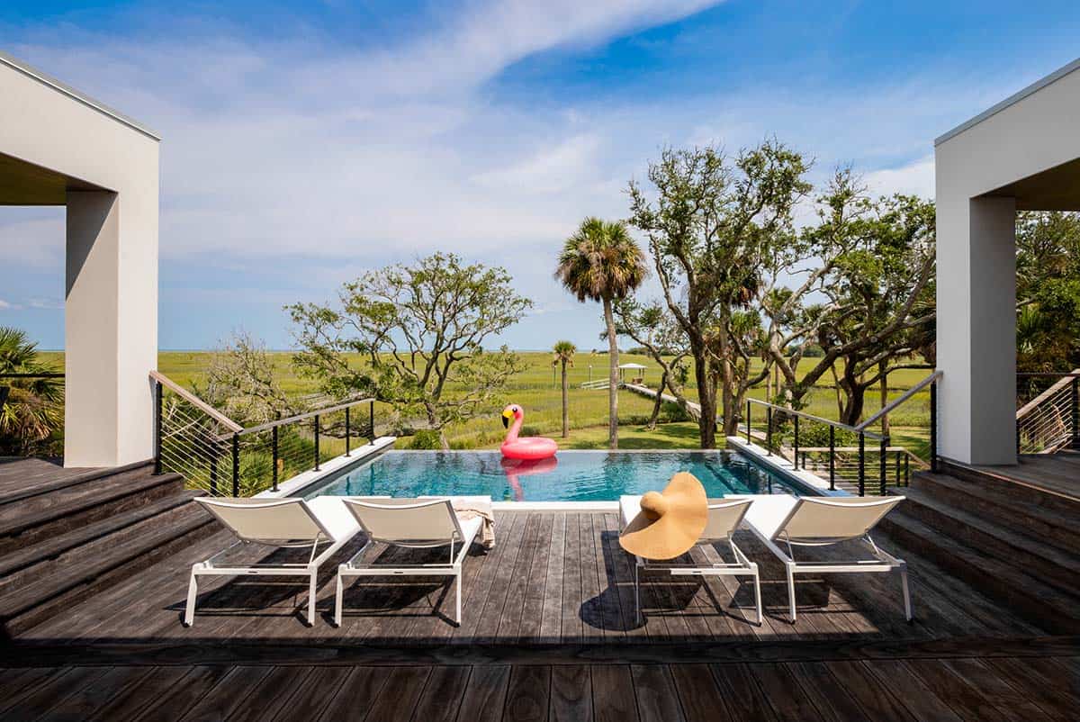 Infinity-edge pool deck with lounge chairs overlooking marsh landscape
